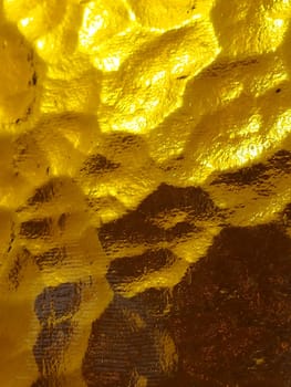 golden yellow corrugated glass with a light and dark background. reflections of light. Corrugated glass, rear light source. Play of glare and reflections on a transparent uneven surface