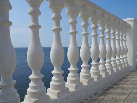 A balustrade with a view of the sea, sky and horizon, a fence consisting of a row of figured baluster posts, connected from above by a railing or a horizontal beam. Railing from curly white posts