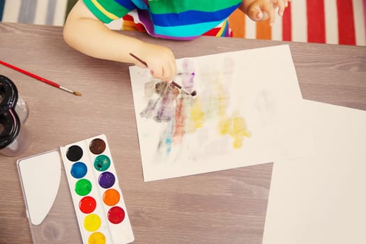 Little child drawing picture by using watercolors indoors. Concept of leisure and kindergarten.