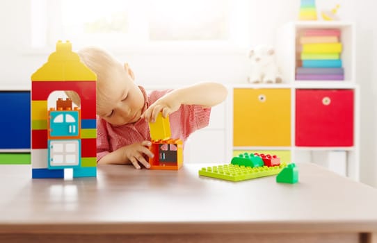 Cute child sitting at the table and playing with constructor. Concept of the kindergarden and leisure.