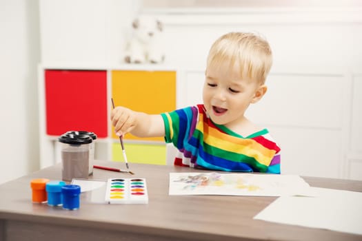 Cute boy drawing picture by using watercolors and couache indoors. Concept of leisure and kindergarten.