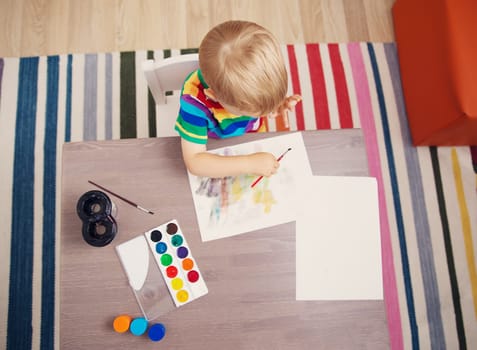 Little boy drawing picture by using watercolors and couache indoors. Concept of leisure and kindergarten.