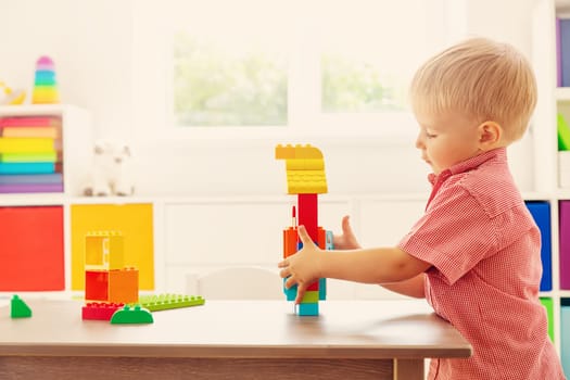 Cute child sitting at the table and playing with constructor. Concept of the kindergarden and leisure.