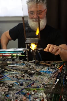 Venice, Italy - September 5, 2022: Glassworker while shaping the glass with a very high temperature flame in its artisan workshop in Venice. Italy