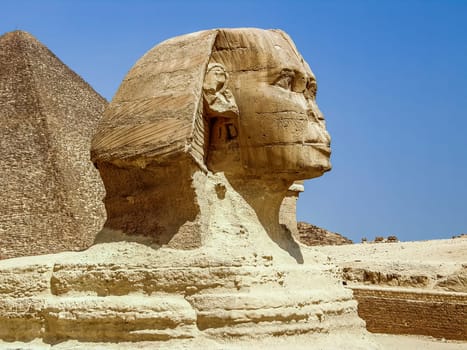 Sculpture of the Great Sphinx against the blue sky. Profile view. The head, part of the body and the top of the ancient pyramid above the back are visible. Egypt. Giza