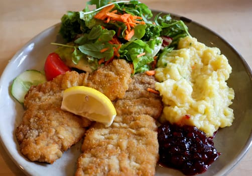 Two Wiener Schnitzels on a plate with sallat and mashed potatoes.