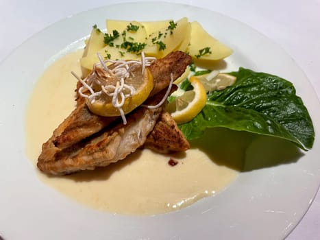 A plate with fish fillet, potatoes and a sour sauce.