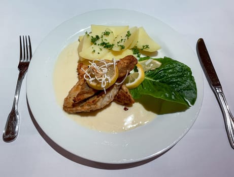 A plate with fish fillet, potatoes and a sour sauce.