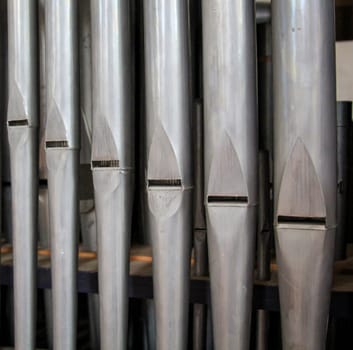 Many organ pipes stand side by side in an organ over a bellows.