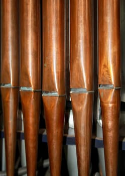 Many organ pipes stand side by side in an organ over a bellows.