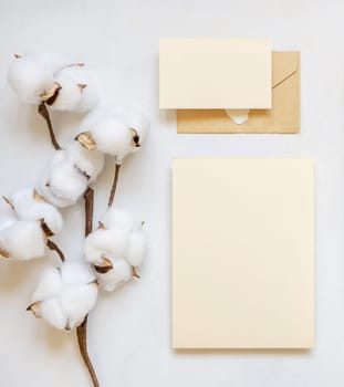Blank cards and envelope with cotton flowers top view on white, mockup. Romantic scene with wedding suite. Bohemian pastel greeting or wedding set