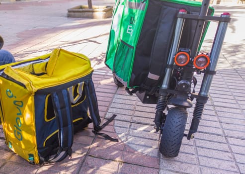 Caceres, Spain - Jan 19th, 2021: Delivery service backpacks and electric kick scooters. Urban background