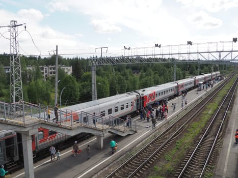Svir, Russia August 6, 2021. Passenger train. Platform with people who got off the train, top view. Rails and sleepers. Stopover. Ladder above the railroad tracks for crossing the road. Summer day.