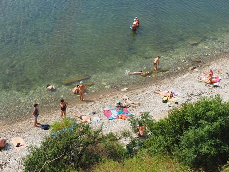 Anapa, Russia, August 23, 2021 Vysokiy Bereg beach or Kamenka. Stone pebbles on the beach. Tourists swim and sunbathe. Summer day. Clear water in the Black Sea. Leisure and tourism at sea