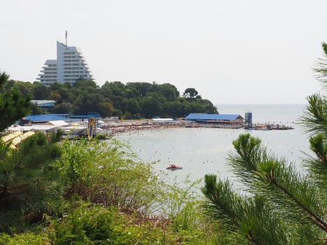Anapa, Russia, August 23, 2021 Vysokiy Bereg beach or Kamenka. Stone pebbles on the beach. Tourists swim and sunbathe. Summer day. Clear water in Black Sea. Leisure and tourism. Pine branches.
