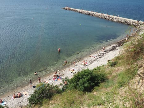 Anapa, Russia, August 23, 2021 Vysokiy Bereg beach or Kamenka. Stone pebbles on the beach. Tourists swim and sunbathe. Summer day. Clear water in Black Sea. Leisure and tourism. Artificial embankment.