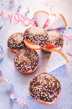 Chocolate Berliner pastry for carnival and party. German Krapfen or donuts with streamers and confetti. Colorful carnival or birthday image