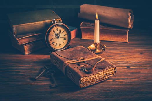 Old antique books with candle and vintage clock on wooden background