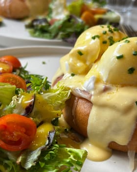 Eggs benedict with hollandaise sauce are served with a side salad for a healthy and satisfying brunch