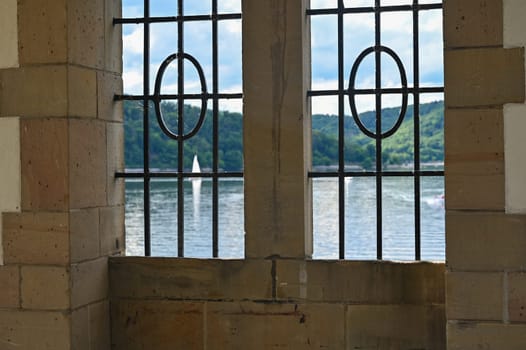 View through a barred window at the Staudam on the Edersee with a sailing ship , in Hesse, Germany