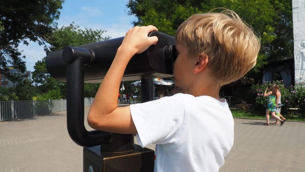 Anapa, Russia, August 23, 2021 A boy looks through an outdoor telescope. A 9-year-old Caucasian child holds a large marine telescope with his hands. The street of the resort town and walking tourists.