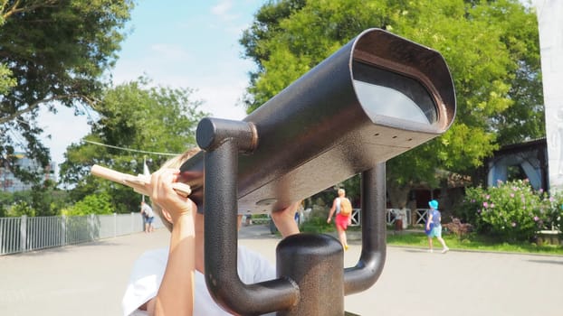 Anapa, Russia, August 23, 2021 A boy looks through an outdoor telescope. A 9-year-old Caucasian child holds a large marine telescope with his hands. The street of the resort town and walking tourists.