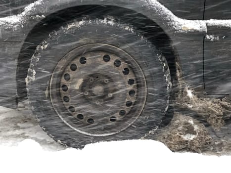 winter road, the car makes its way through a snowstorm, the wheel in a snowdrift
