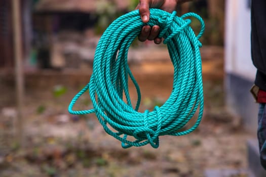 Green rope in the hand of a man on a blurred background.