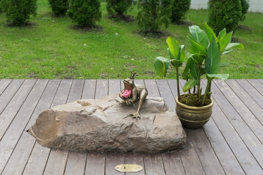 A bronze statuette of Princess Frog, sitting on a boulder in the park (side view)