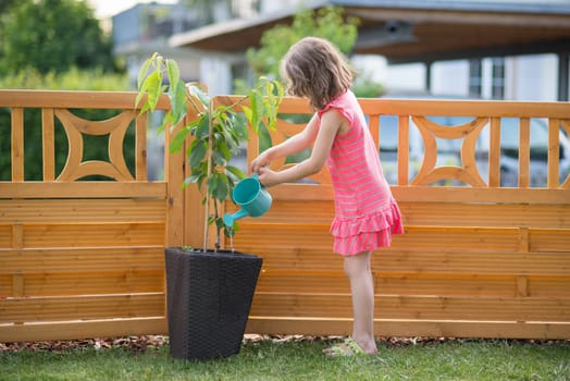 Happy little girl watering plants in the garden
