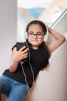 Cute happy girl with glasses listening to music on headphones