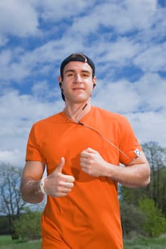 Frontal upper body view of a young man in an orange T-shirt on paved footpath joyfully running towards the camera