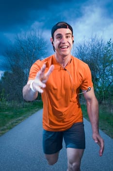 Frontal upper body view of a young man in an orange T-shirt on paved footpath joyfully running towards the camera