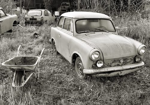 an old broken car of the type "Trabant"" stands in a garden and rots"