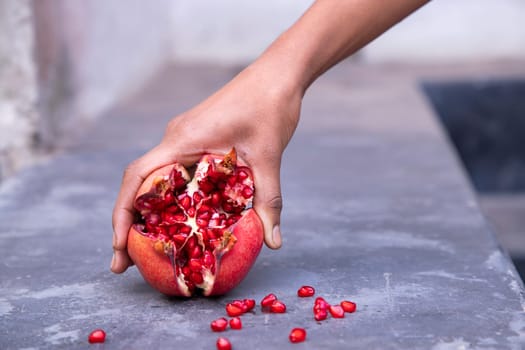 Ripe pomegranate fruit in woman's hand on concrete background