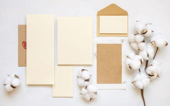 Blank cards and envelope with cotton flowers top view on white, mockup. Romantic scene with wedding suite. Bohemian pastel greeting or wedding set