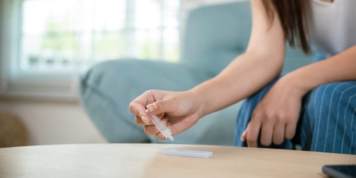 Close up woman hands using rapid antigen test kit for selftest, female four drops of liquid to perform fast coronavirus ATK self test at home in living room on sofa after lockdown and Home Isolation