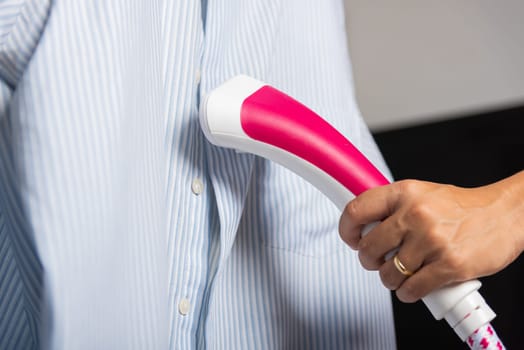 Close up of woman using electric hand steam generator while it is hot and steam comes out for clothes shirt at house, Household and home equipment for housework, concept of linen care