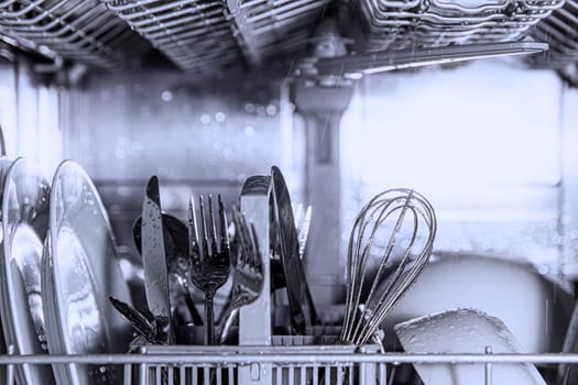 Front view of open automatic stainless steel built-in fully integrated top control dishwasher range machine with clean utensils, cutlery, glasses, dishes, plates inside in modern home kitchen