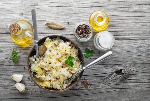 Homemade sauerkraut with black pepper and parsley in wooden bowl on rustic background. Top view. Copy space.