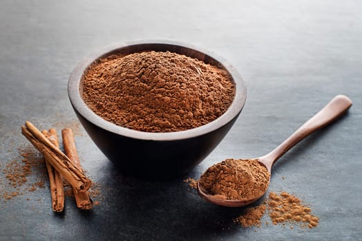 Aromatic cinnamon sticks with cup and spoon with powder on grey background close up