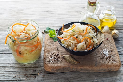Homemade sauerkraut with carrot, black pepper and parsley in bowl on rustic background. Top view. Copy space