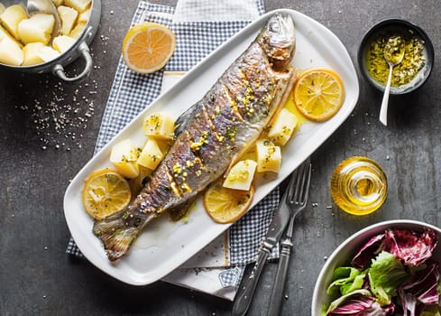 Roasted traditional river trout with salad, potatoes and (garlic, parsley) sauce on grey table background