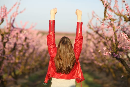 Back view of a woman in red jacket celebrating vacation in a flowered field
