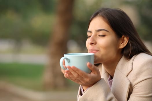 Woman at sunset in winter smelling coffee in a park