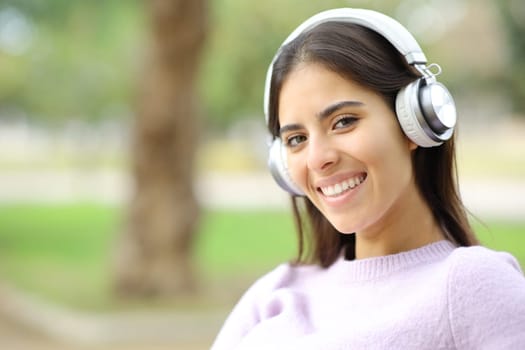 Happy woman wearing headphones looks at camera sitting in a park