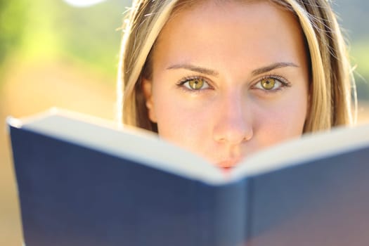 Front view of a beautiful woman reading a book looking at you with amazing eyes