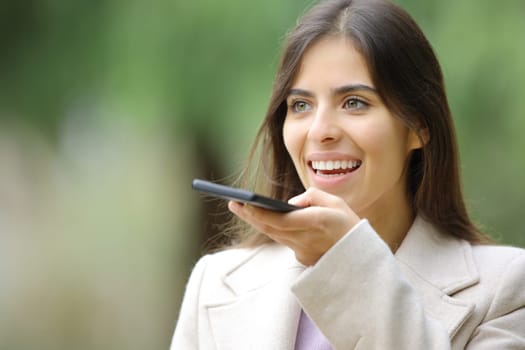 Woman in winter dictating message on phone walking in a park