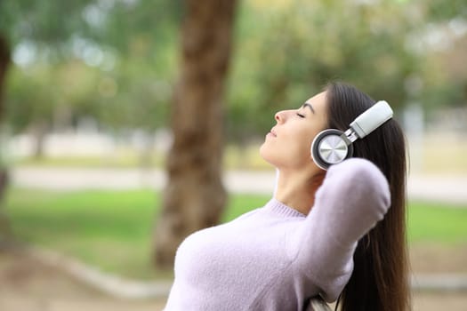 Side view portrait of a woman resting listening to music on bench in a park