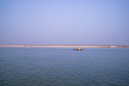 landscape view of Padma river on a fishing boat with a sand island under the blue sky
